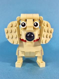 a dog made out of legos sitting on a blue surface with its eyes wide open