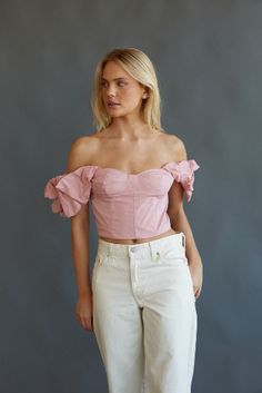 a woman standing in front of a gray wall wearing white pants and a pink top