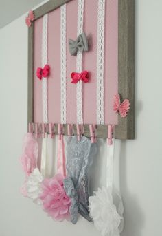 a pink and white wall hanging with bows on it's hooks, made out of fabric