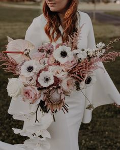 a woman holding a bouquet of flowers in her hands and wearing a white dress with long sleeves