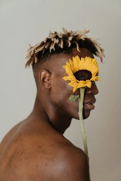 a man with dreadlocks holding a sunflower to his face