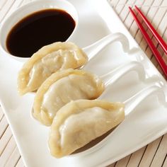 three dumplings on a white plate with chopsticks next to it and sauce