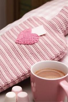 a pink knitted pillow with a heart on it next to a cup of coffee