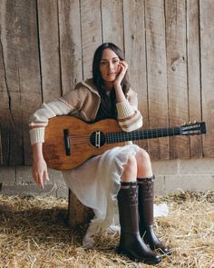 a woman sitting on top of hay holding a ukulele