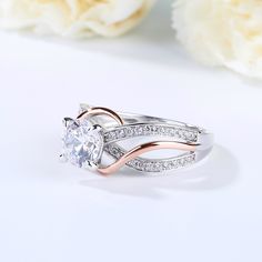 a white and rose gold ring with diamonds on the side, sitting next to flowers