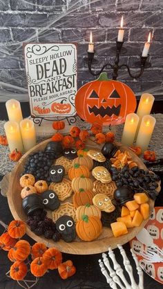 a wooden plate topped with lots of halloween cookies next to candles and pumpkins on top of a table