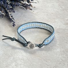 A Hematite stacker bracelet on soft silver leather, combined with pastel blue beads and finished off with a silver TierraCast lotus flower button. A perfect gift for a loved one or simply a treat for yourself! ✨ - Measures 17cm/6.75"  - Has one extra loop which adds another 2.5cm/1" if needed (if not needed the loop can be carefully cut off, leave a 1.5cm tail) - Soft silver leather - 3mm round silver Hematite - 3mm faceted Czech glass - Jewellery grade thread - Silver TierraCast lotus flower button Hematite: Protects, stabilises and grounds. Increases confidence, clarity and mental organisation. Shifts negative energy out of the aura (Root Chakra). This piece comes in an organza bag and wrapped in tissue, ready to give 💕 https://www.etsy.com/uk/shop/LittleGemsbyMel For real life events a Adjustable Blue Wrap Bracelet For Everyday, Adjustable Hand Wrapped Blue Leather Bracelet, Elegant Adjustable Blue Leather Bracelet, Elegant Blue Adjustable Leather Bracelet, Elegant Blue Leather Bracelet For Gift, Adjustable Silver Leather Bracelet With Round Beads, Adjustable Silver Spiritual Wrap Bracelet, Adjustable Silver Beaded Leather Bracelet, Adjustable Silver Leather Bracelet Hand Wrapped