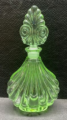 a green glass perfume bottle sitting on top of a white countertop next to a black wall