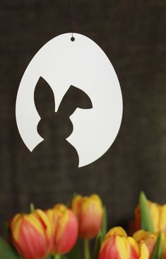 a paper cutout of a bunny is hanging from a string with tulips in the foreground