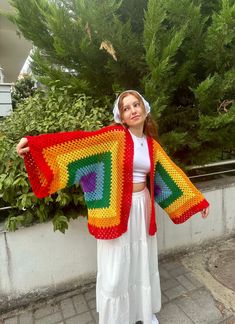 a woman is holding up a colorful crocheted blanket