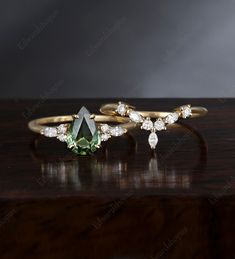 two gold rings with green and white stones on top of a wooden table next to each other