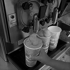 two cups of ice cream are being filled into an espresso machine, while someone reaches for one cup