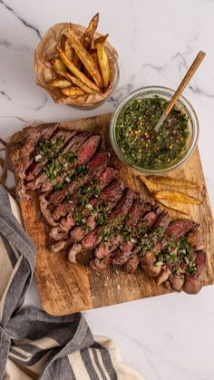 steak with pesto sauce and french fries on a wooden cutting board next to it