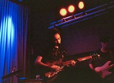 two people are playing guitars in front of microphones and stage lights at the same time