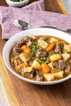 a bowl of beef stew with carrots and celery on a cutting board