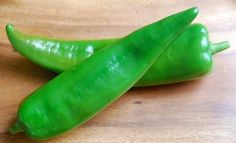 two green peppers sitting on top of a wooden cutting board