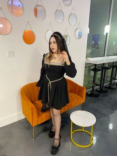 a woman in a black dress standing next to an orange chair