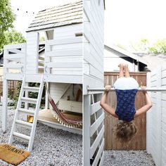 a girl climbing up the side of a white wooden house with a hammock attached to it