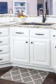 a kitchen with white cabinets and granite counter tops, along with an area rug on the floor