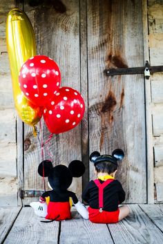 two mickey mouse dolls sitting next to each other with balloons in the shape of mice