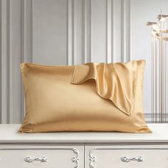 a gold pillow sitting on top of a white table next to a lamp and dresser