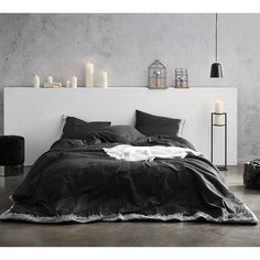 a black and white bedroom with candles on the headboard, bed linens in dark colors