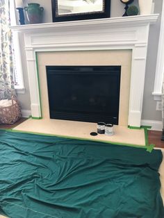 a living room with a fireplace covered in green tarp and two paint cans on the floor