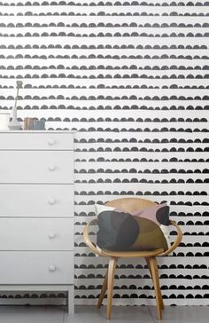 a chair sitting in front of a white dresser next to a wall with black circles on it