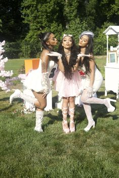 three beautiful young women standing next to each other in front of a white table and chairs