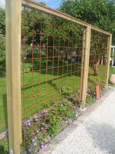 the fence is made of metal wire and has flowers growing on it, along with gravel