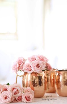 some pink roses are in gold cups on a table