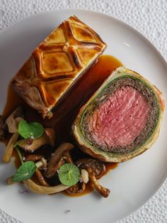 a white plate topped with meat and vegetables next to a roll on top of a table