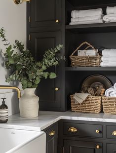 a bathroom with black cabinets and white towels on the shelves, plants in a basket