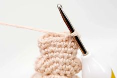 a crocheted object with a knitting needle in the middle and a white ball of yarn next to it