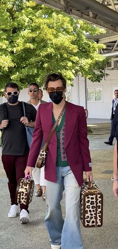 two people walking down the street with suitcases in their hands and one person wearing a face mask