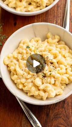 two white bowls filled with macaroni and cheese on top of a wooden table