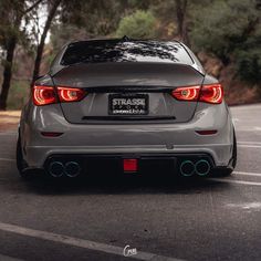 the rear end of a gray car parked in a parking lot next to some trees