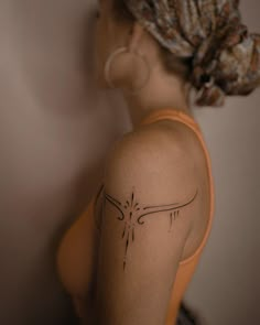 a woman with a tattoo on her back shoulder and an orange tank top is standing in front of a wall