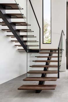 a modern staircase with glass railing and wooden handrails in an empty room next to a window