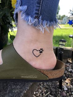 a small heart tattoo on the foot of a woman with a paw print in it