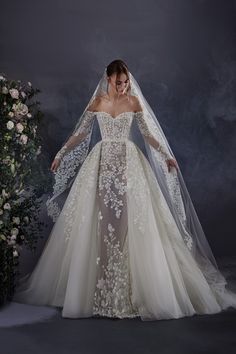 a woman in a wedding dress with a veil on her head and flowers behind her