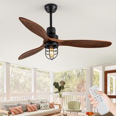 a person holding a remote control in front of a ceiling fan