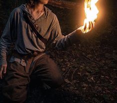 a man sitting in the woods holding a lit fire stick up to his face with both hands