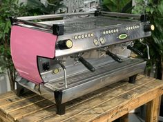 a pink coffee machine sitting on top of a wooden table