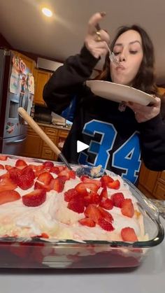 a woman holding a plate with strawberries on it in front of a cake dish