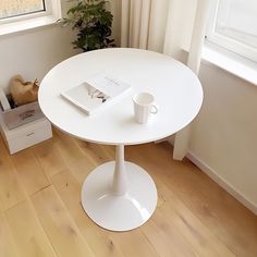 a white table with a book and cup on it in front of a large window