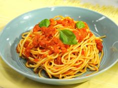 a blue bowl filled with spaghetti and sauce on top of a yellow table cloth next to a fork