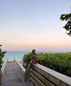 a woman sitting on a wooden bench next to the ocean at sunset with her arms crossed