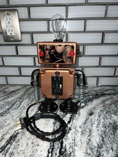 an old fashioned robot sitting on top of a counter next to a light switch and plugged in