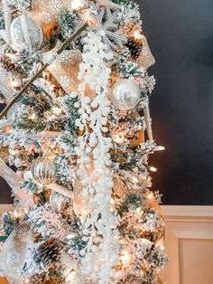 a white christmas tree with silver and gold ornaments on it's branches is decorated with snowflakes